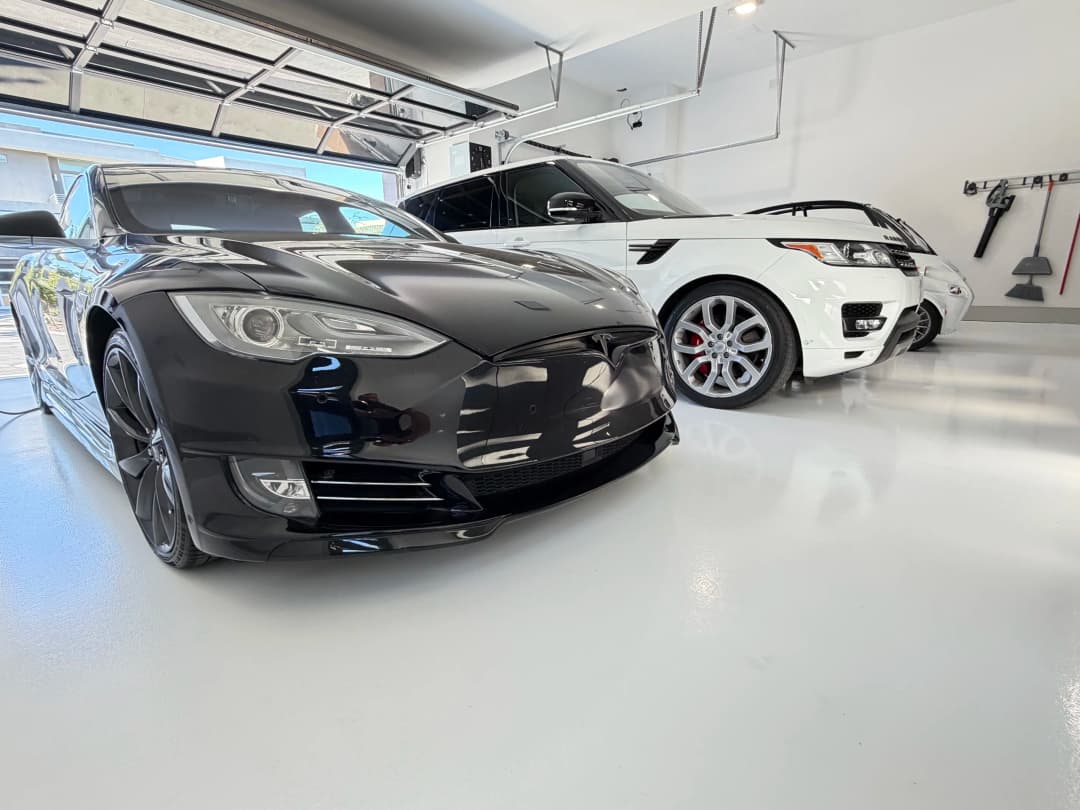 Black Tesla Model S parked in a modern garage next to a white luxury SUV.