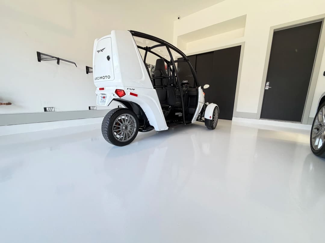 White electric trike parked in a modern garage with sleek flooring and minimalist design.