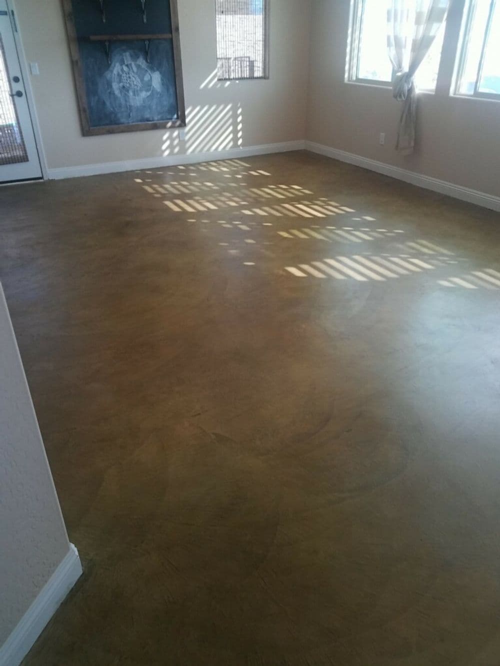 Polished concrete floor in a sunlit room with large windows and decorative wall.