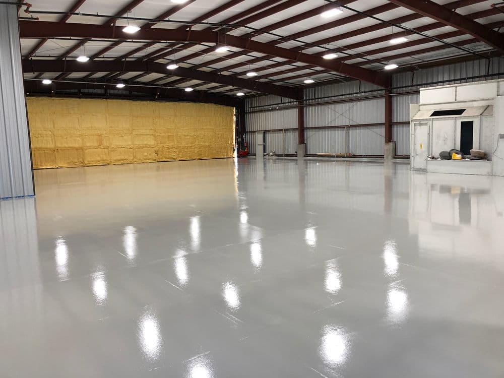 Large industrial warehouse with freshly coated gray epoxy floor and steel beams.