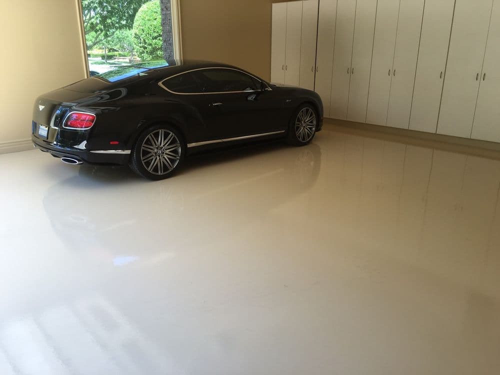 Luxury black Bentley parked in a clean, spacious garage with white cabinets.