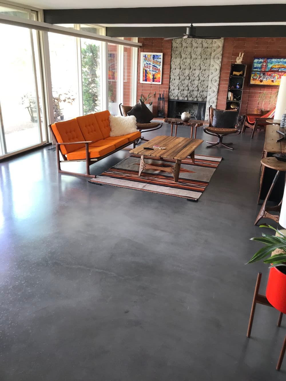 Modern living room with orange sofa, wood coffee table, and stylish decor on polished concrete floor.