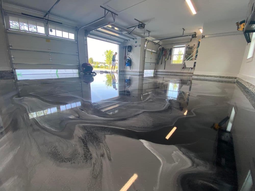 Modern garage with glossy black epoxy floor and workers applying finishing touches.