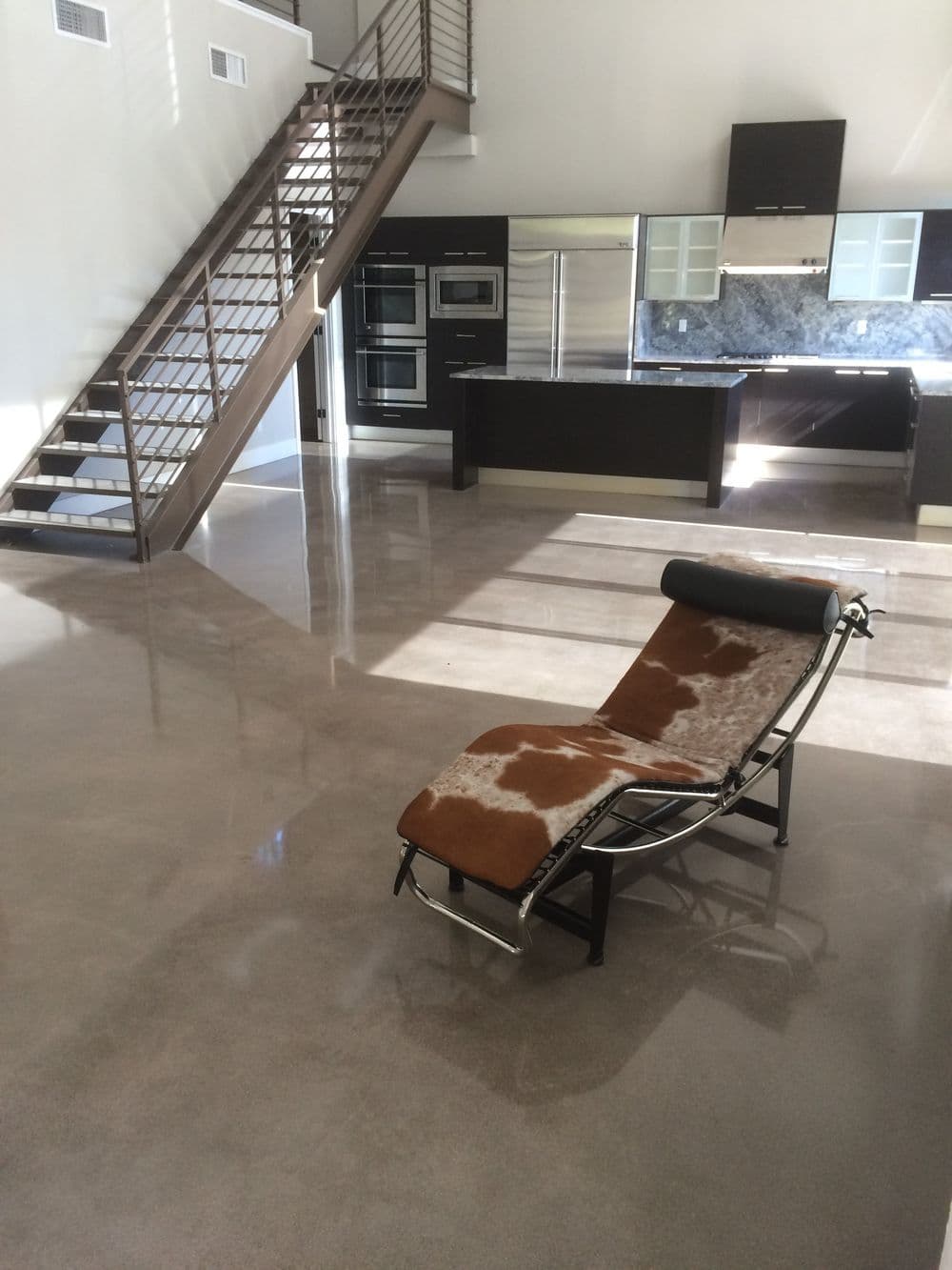 Modern living room with polished concrete floor, stylish lounge chair, and contemporary kitchen.