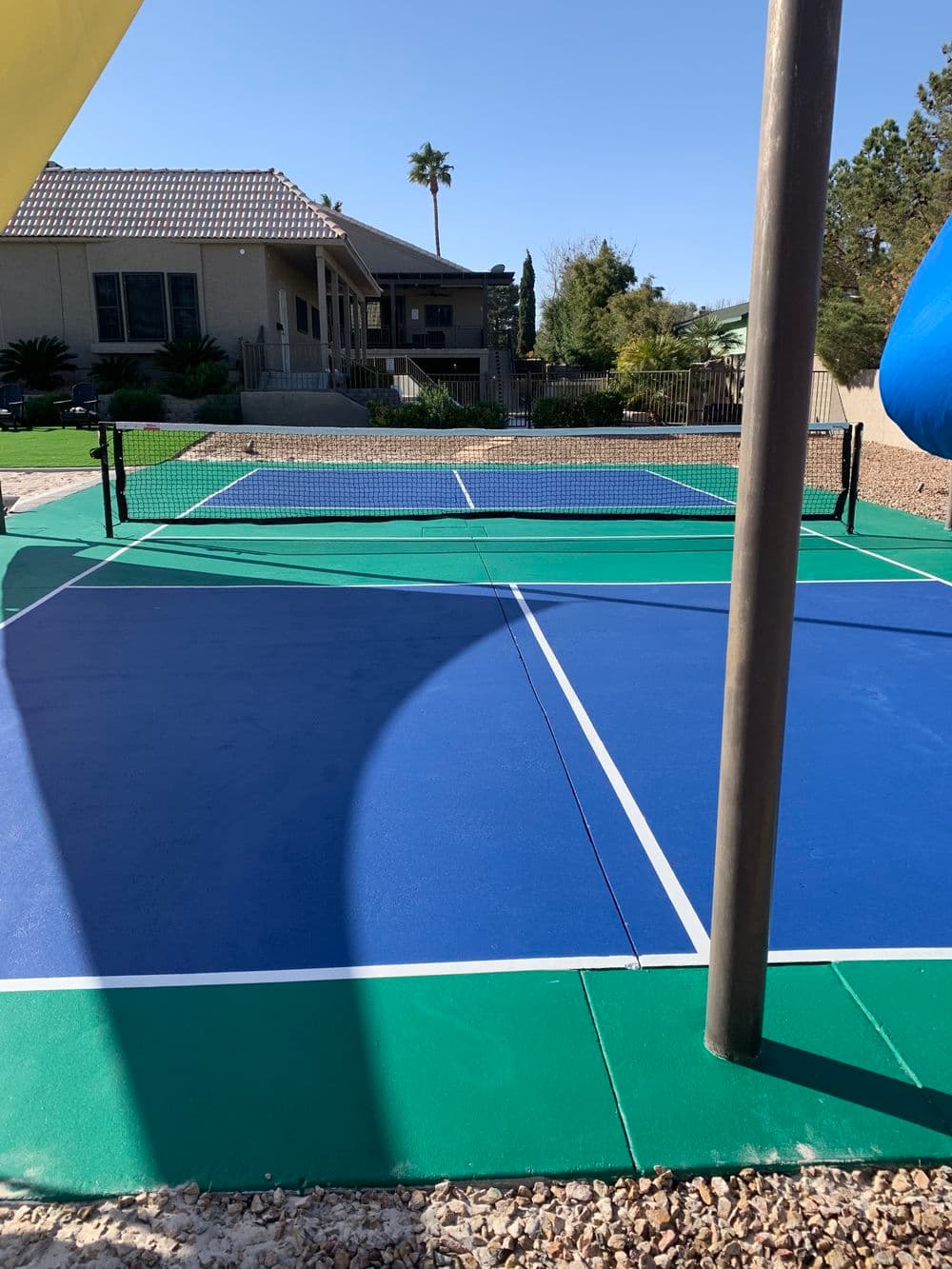 Residential pickleball court with blue and green surfaces, set against a sunny backyard.