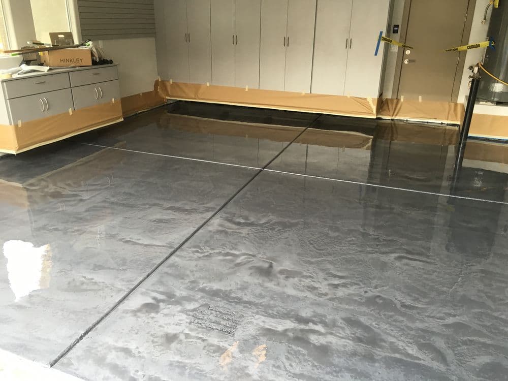 Freshly poured concrete garage floor with protective tape and cabinetry in the background.