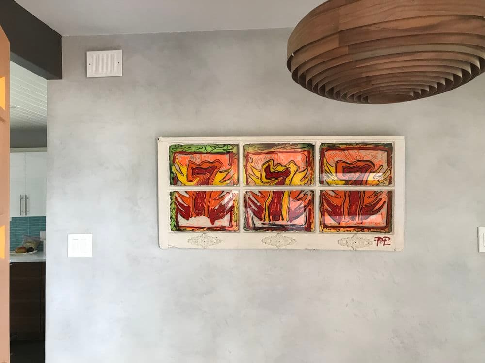 Colorful abstract artwork displayed on textured wall with modern wooden pendant light.