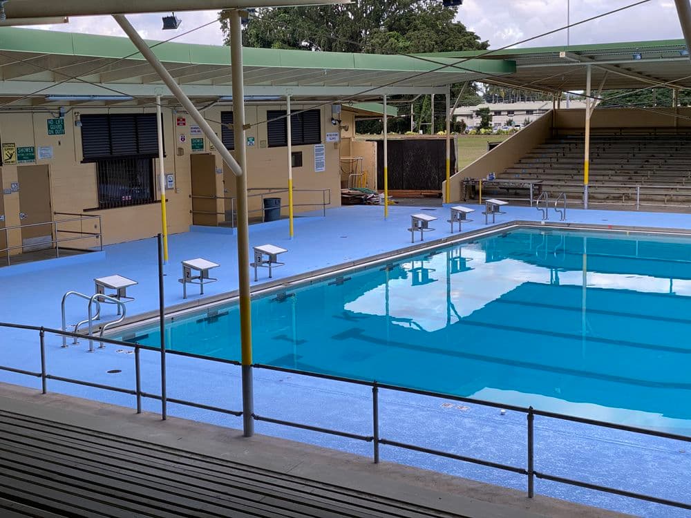Olympic-sized swimming pool with diving boards and shaded seating area nearby.