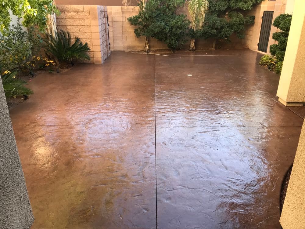 Stamped concrete patio in a residential backyard surrounded by lush greenery.