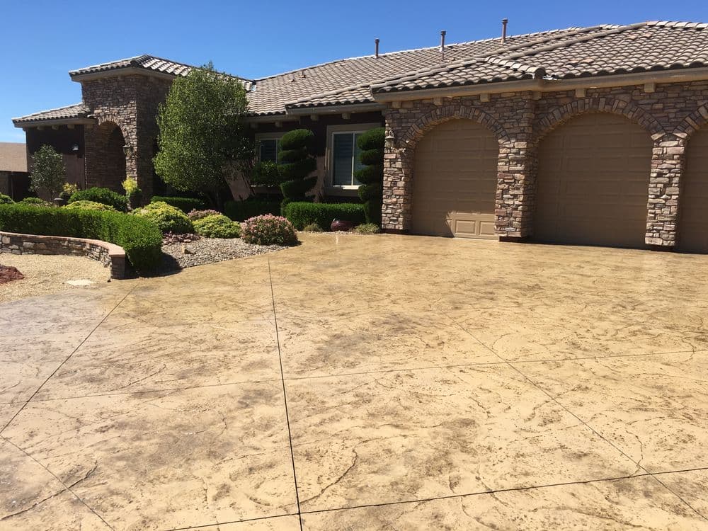 Stylish home with stone accents and stamped concrete driveway under clear blue sky.