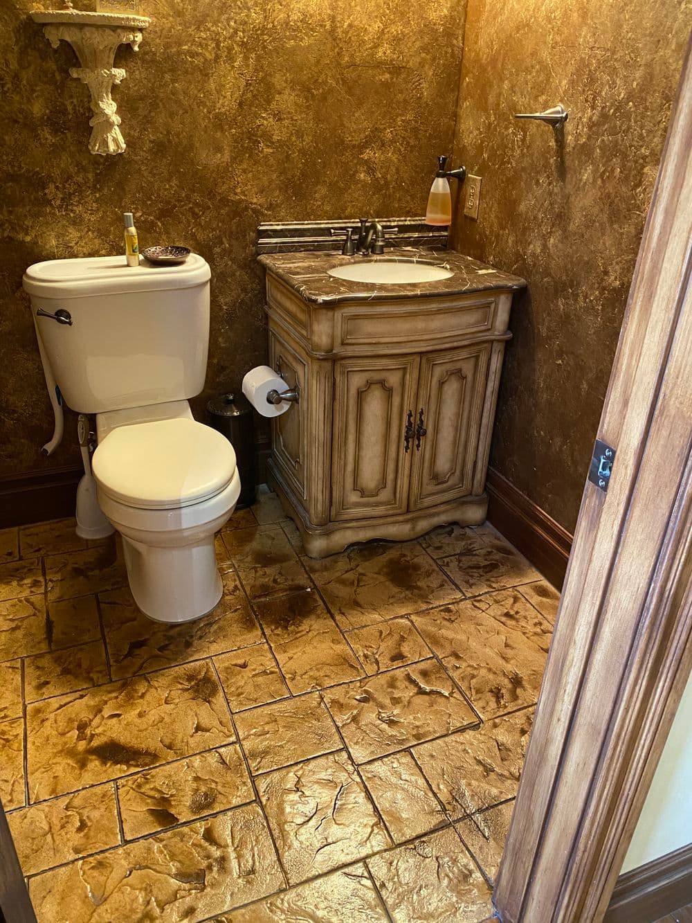 Elegant bathroom with ornate vanity, stone-textured flooring, and modern toilet.