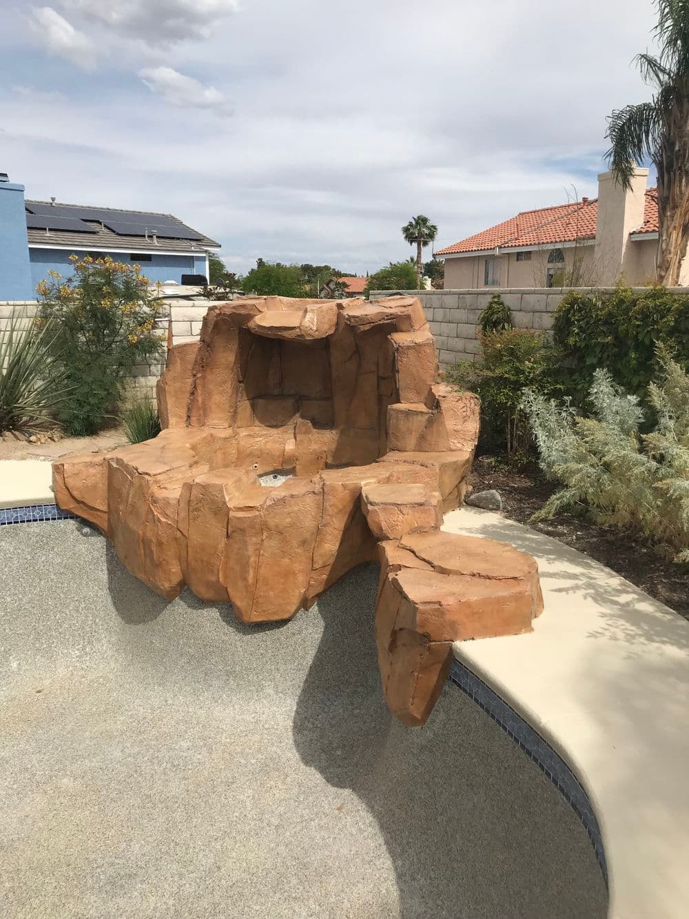 Natural rock formation water feature in a residential poolscape with landscaped surroundings.