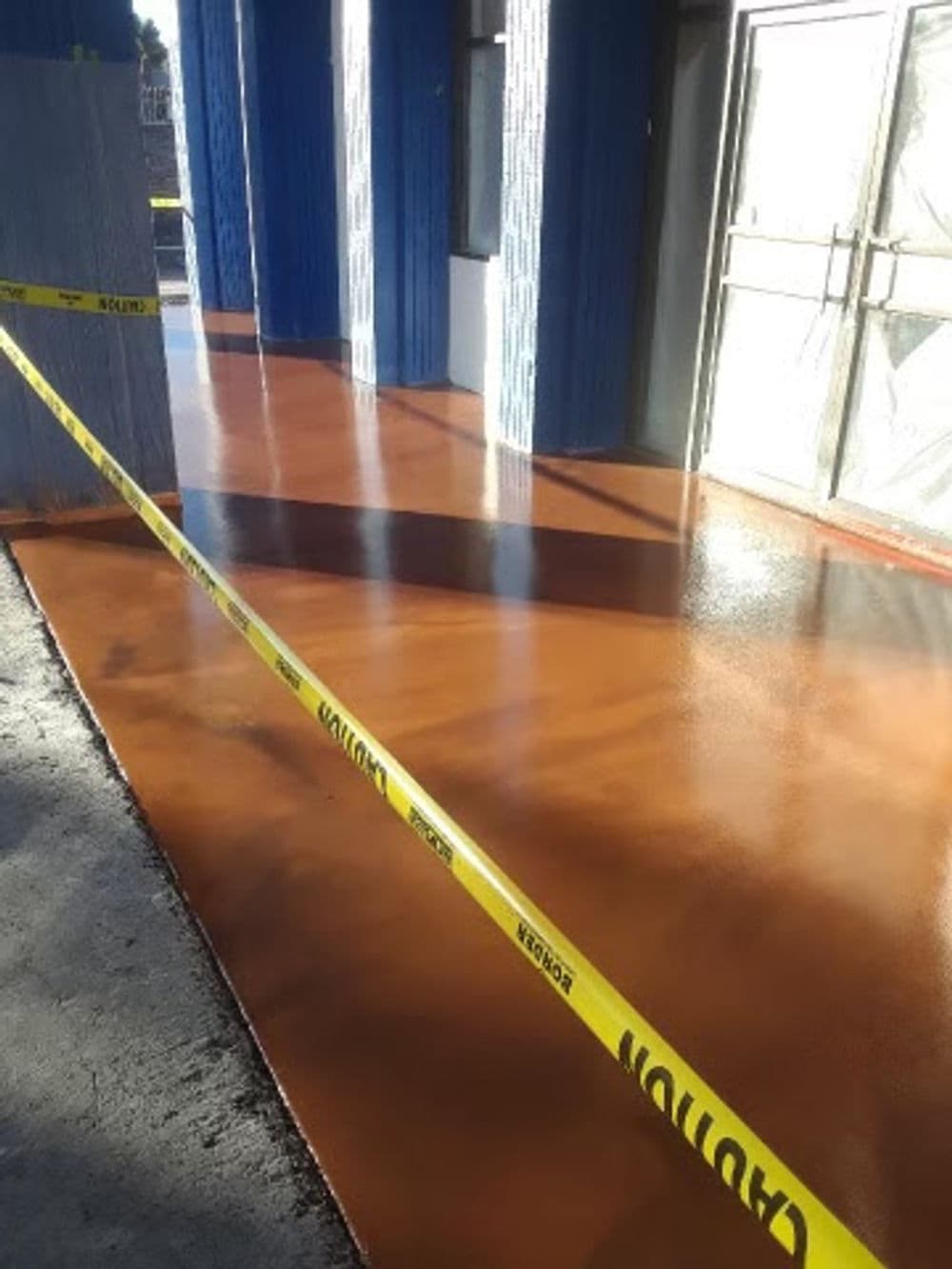 Floor with wet finish and caution tape in front of a building entrance.