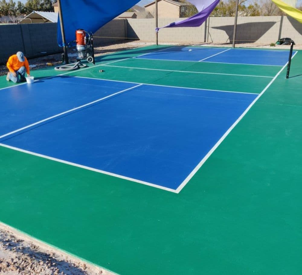 Newly painted tennis courts with blue surfaces and green trim, surrounded by shade structures.