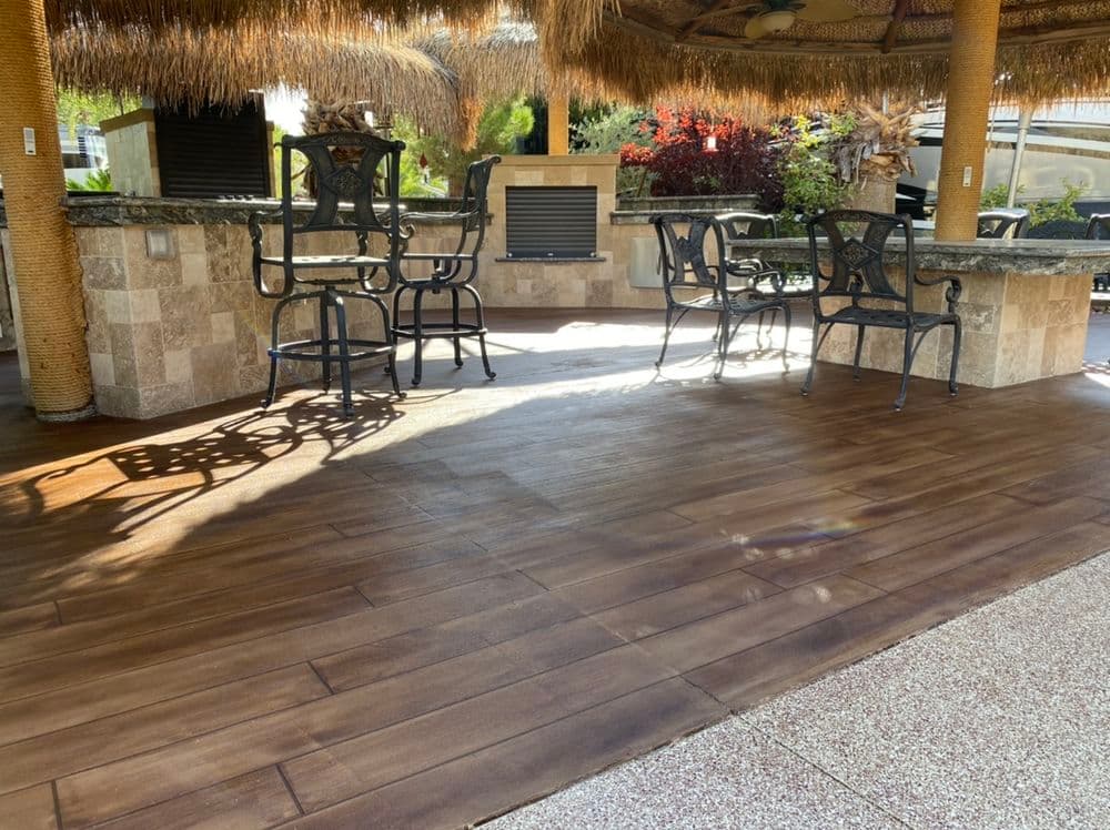 Outdoor patio with wooden flooring, wicker bar stools, and stone outdoor kitchen area.