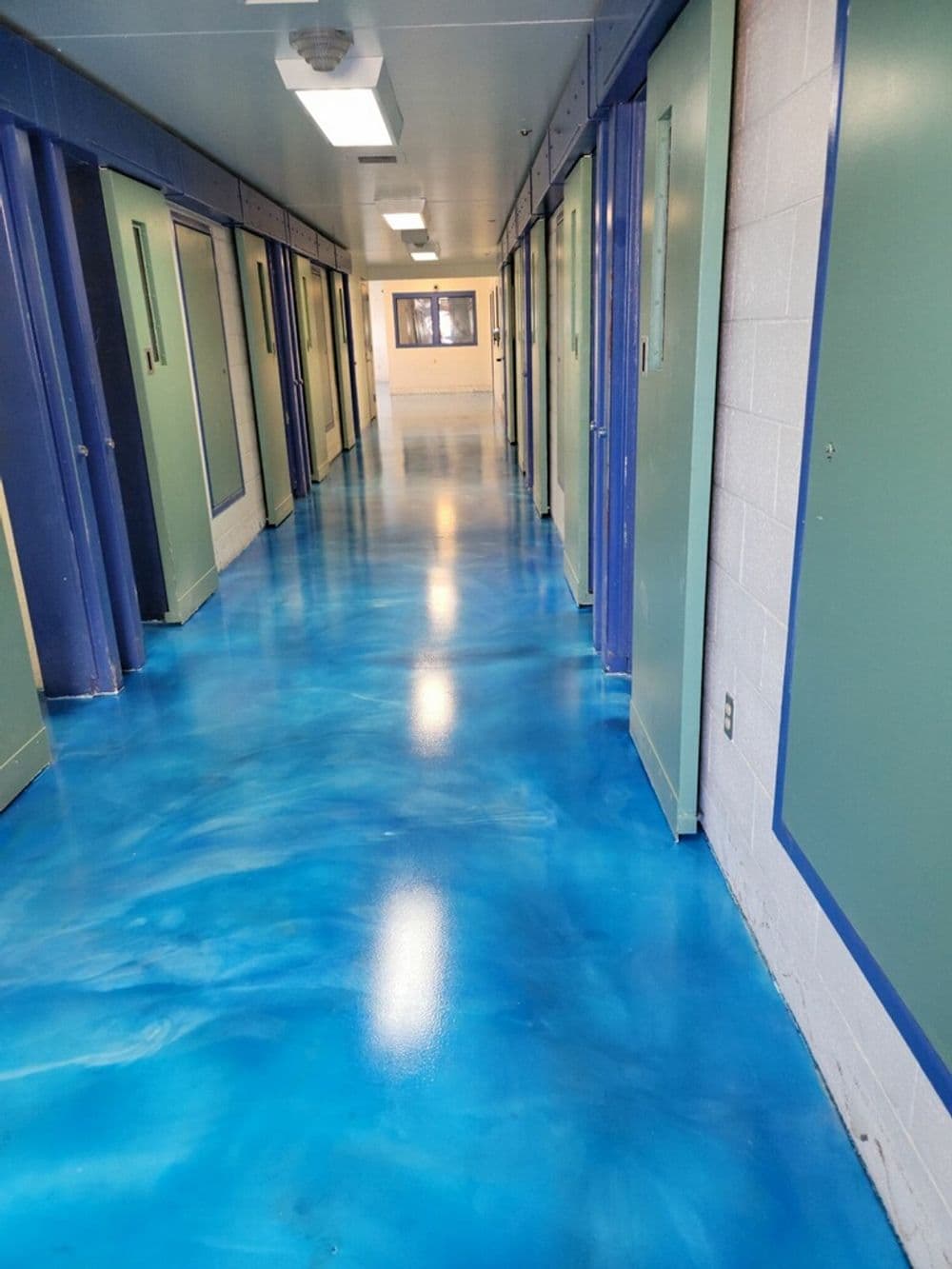 Vibrant blue floor in a hallway with green doors and bright overhead lighting.