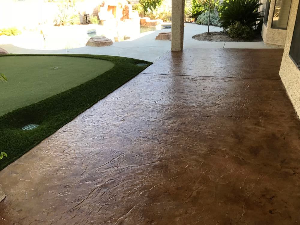 Decorative stamped concrete patio leading to artificial turf putting green in outdoor space.