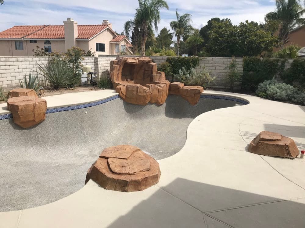 Backyard pool with rocky ledges, palm trees, and a spacious patio area. Ideal for relaxation.