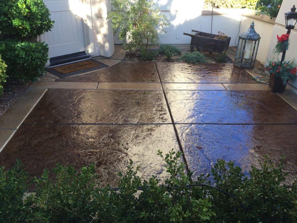 Textured concrete patio with decorative edges, surrounded by greenery and outdoor decor.