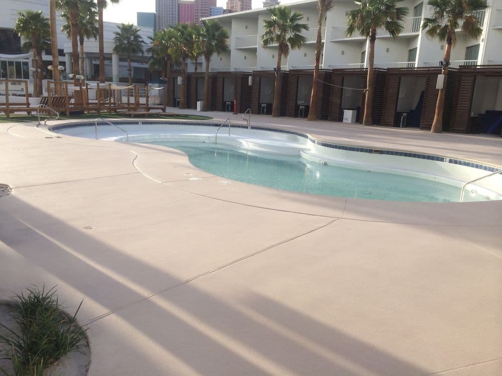 Modern pool area with palm trees and lounge chairs, featuring clear water and a sunny atmosphere.