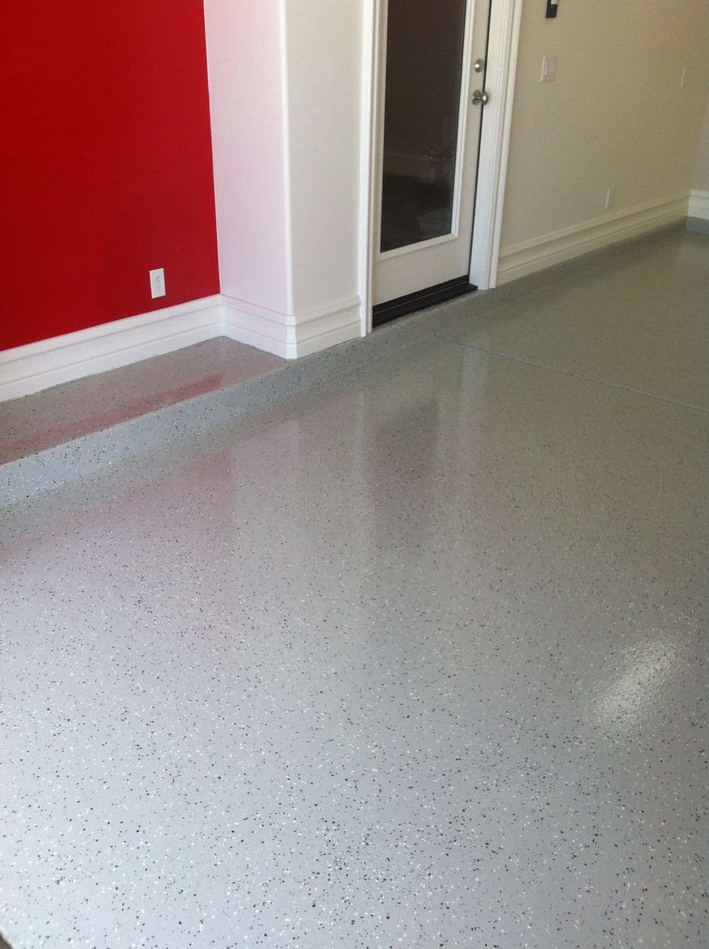 Shiny gray epoxy flooring in a modern room with a red accent wall and glass door.