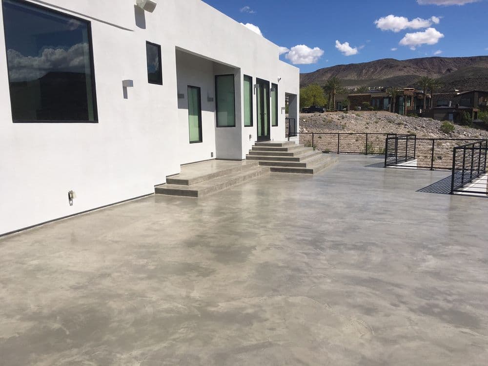 Modern home exterior with concrete patio, steps, and large windows against a mountain backdrop.
