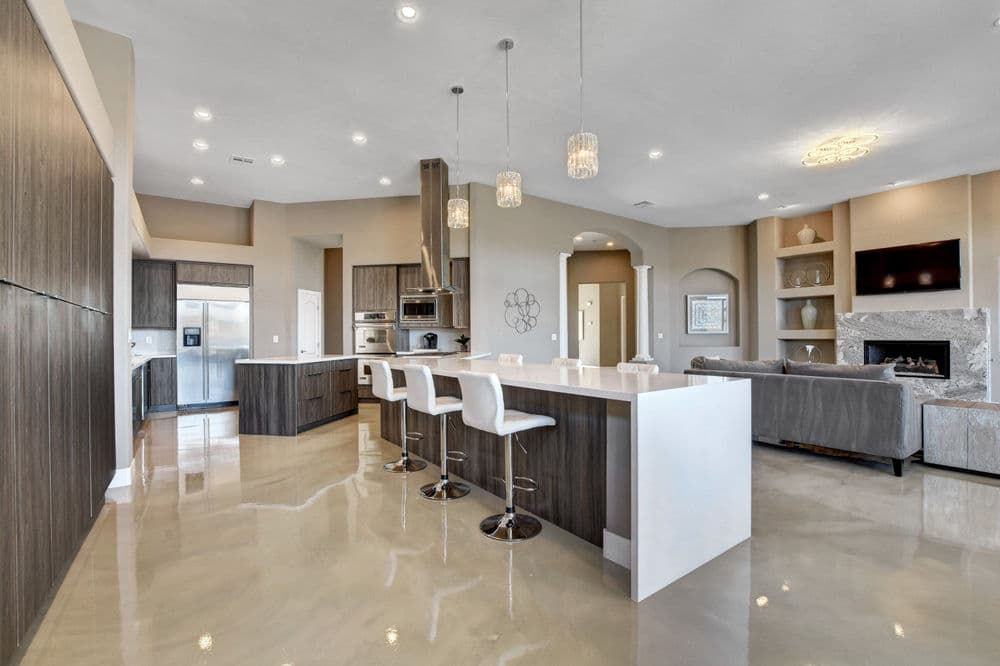 Modern kitchen with island bar, pendant lights, stainless steel appliances, and polished concrete floor.
