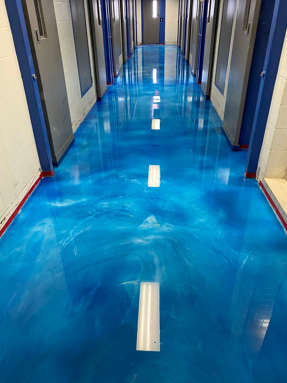 Vibrant blue epoxy floor in a well-lit corridor with metal doors. Modern design and aesthetic appeal.