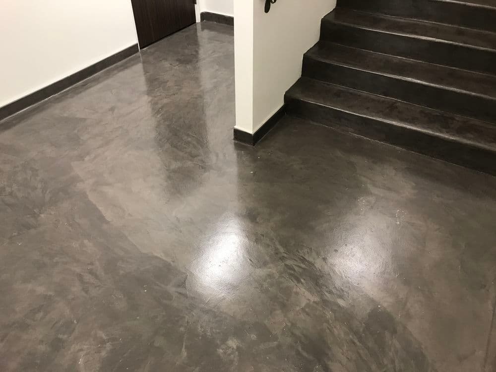 Modern polished concrete floor in a hallway with stairs, enhancing interior aesthetics.