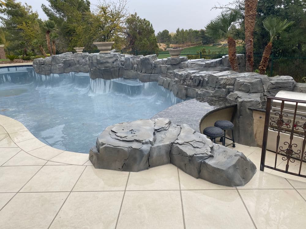 Luxury pool with rock formations, tiled deck, and lush landscaping in a tranquil setting.