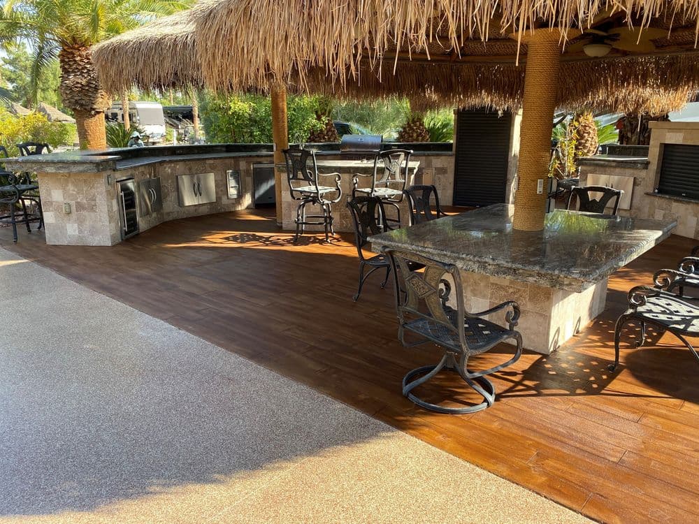 Outdoor patio with a tiki hut, stone tables, and chairs, surrounded by lush greenery.