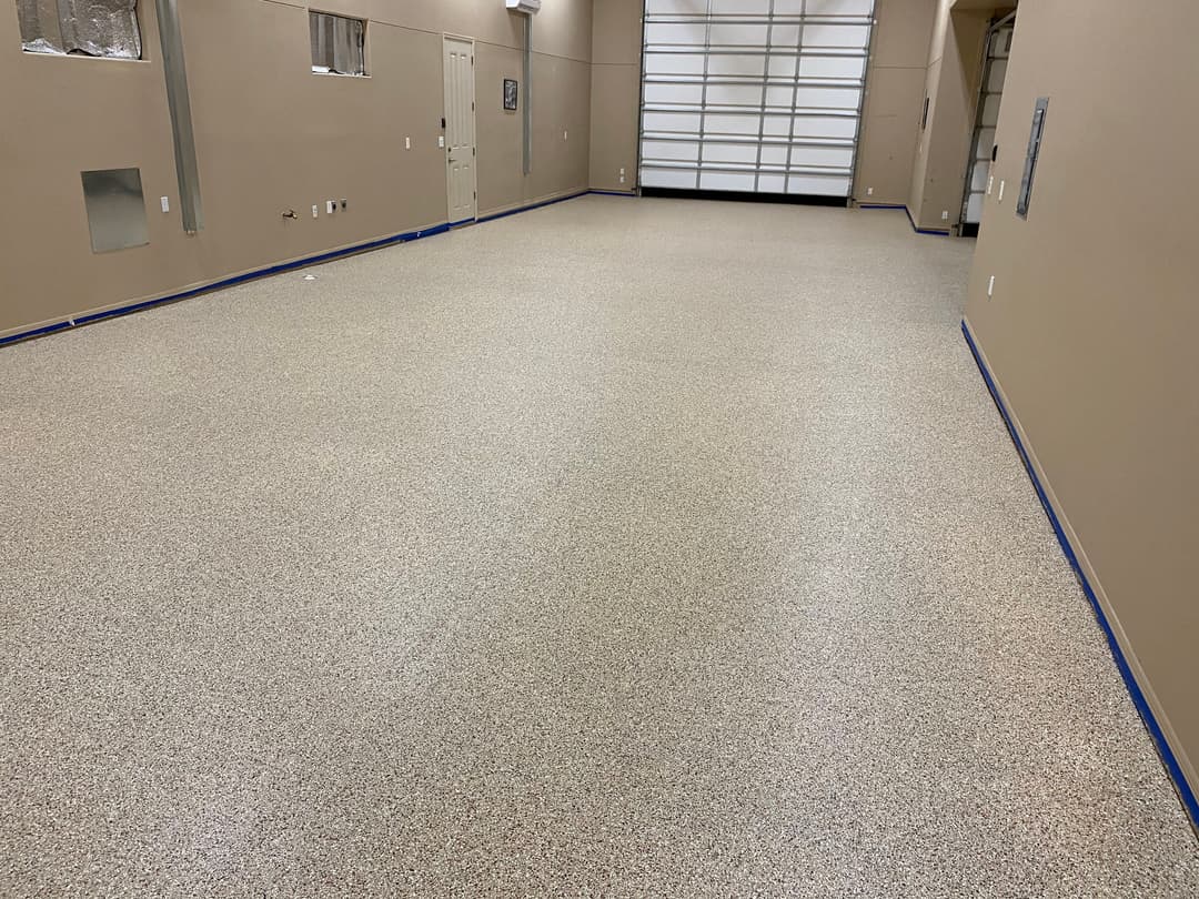 Spacious garage interior with a polished, speckled epoxy floor and beige walls.